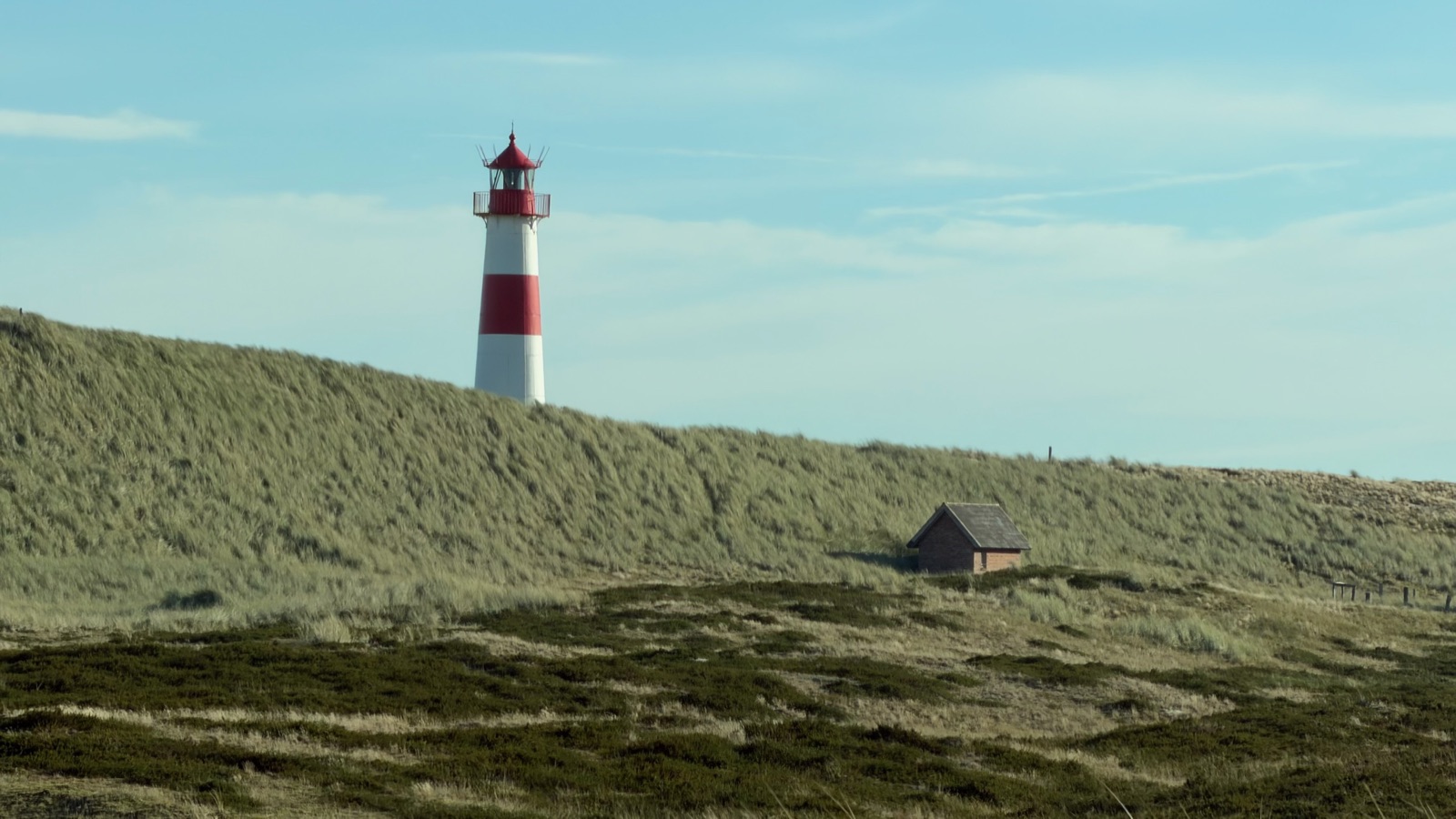 Leuchtturm List-Ost hinter einem Reetdachhaus in den Dünen